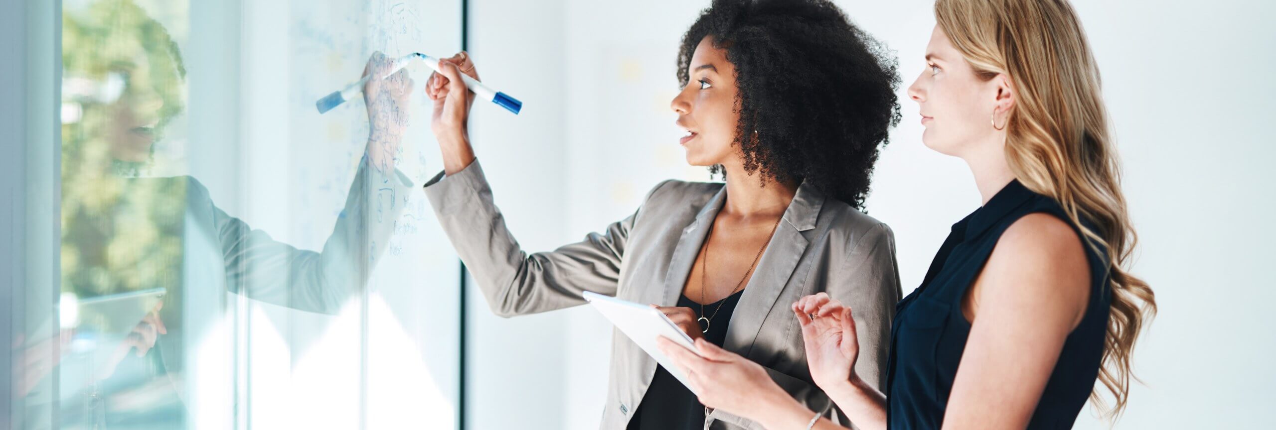 Two professional women analyze a whiteboard, benefiting from Textkernel's business development use cases for staffing agencies.